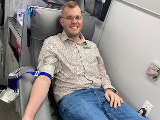 Smiling man with glasses sitting in a blood donation chair, his arm prepared for donation.