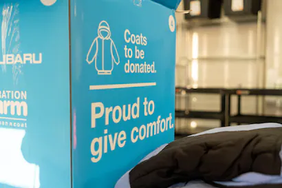 Bright blue Subaru Proud to Give Comfort donation box for coats, with text 