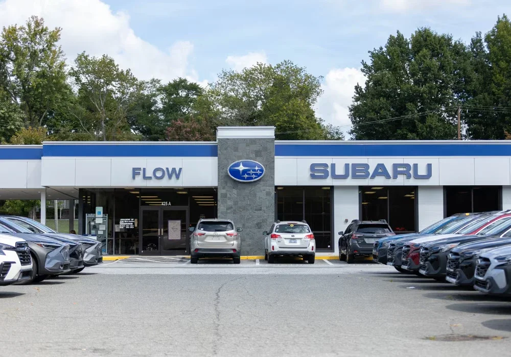 Flow Subaru dealership exterior with new cars parked in front under a blue sky.
